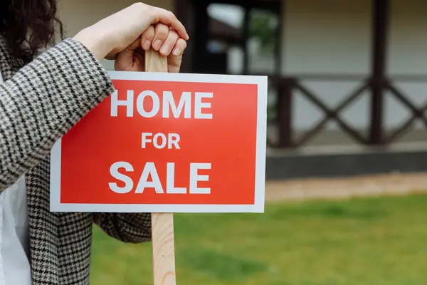Red "Home for Sale" sign on a wooden post in a front yard