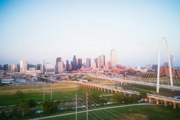 Downtown Dallas skyline at sunset seen across the Trinity River, with the Margaret Hunt Hill Bridge arch