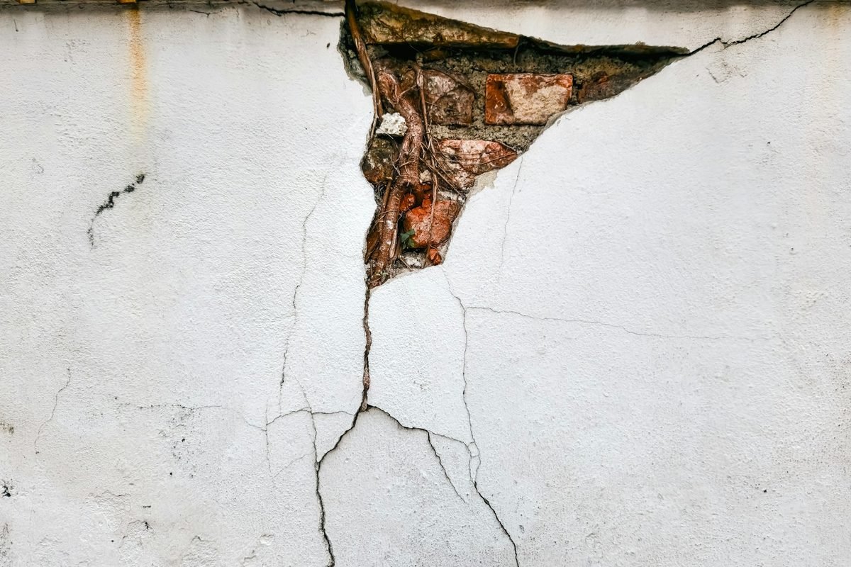 Deep crack running through a plastered wall and exposing the brick underneath, a common sign of foundation movement