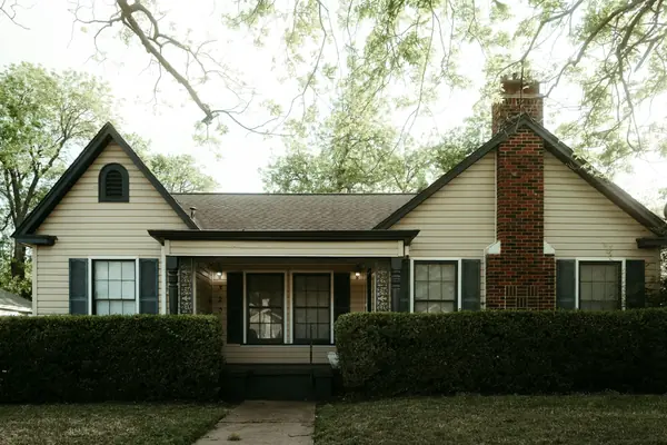 Older single-story family home with a brick chimney, front porch, and mature shade trees